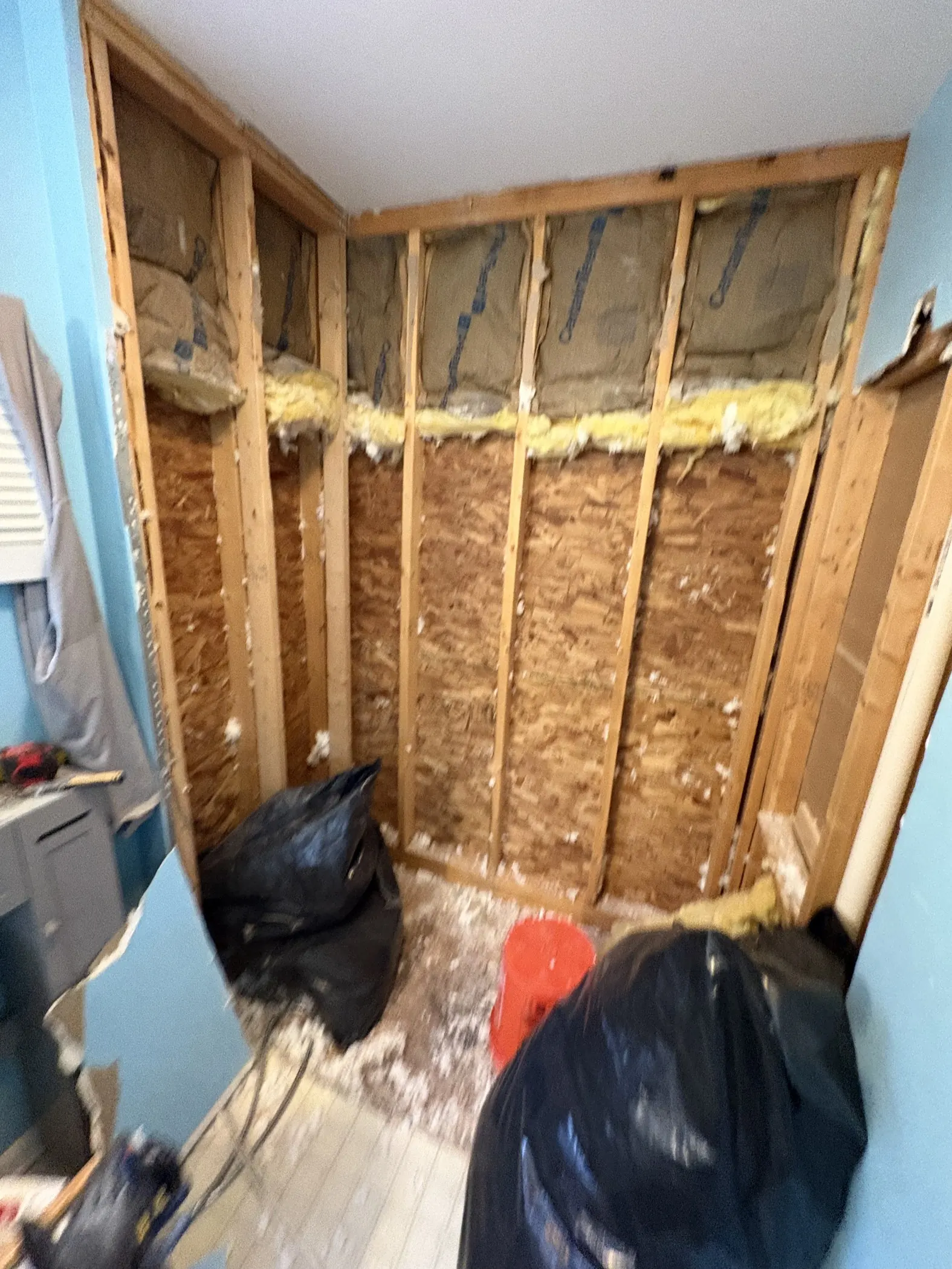 A bathroom interior with wall finishes removed, exposed framing and materials on the floor.