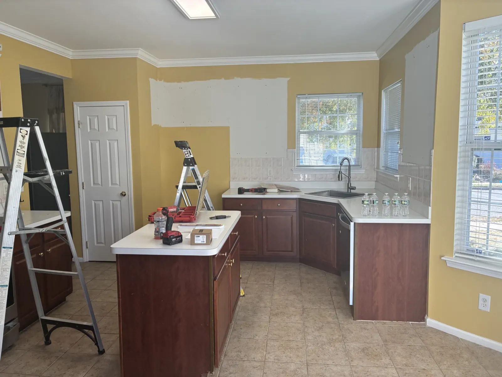 Kitchen at the start of renovation, with upper cabinets removed and lower wood cabinets remaining.
