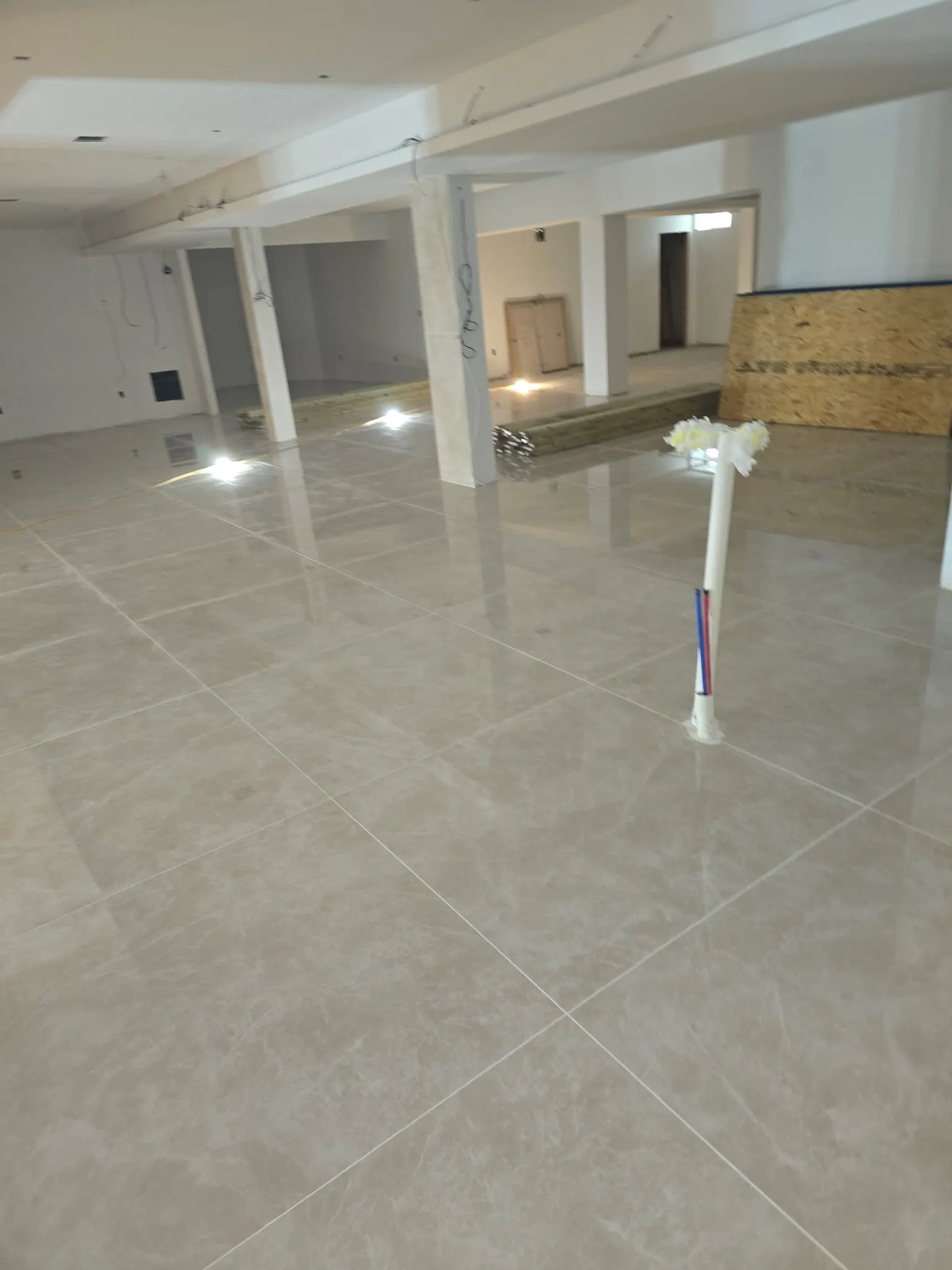 An open interior with tile flooring, unfinished ceiling areas and temporary work lights.